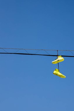 Elektrik kablolarına sarı ayakkabılar asmak, arka planda mavi gökyüzü olan elektrik hattına spor ayakkabıları asmak