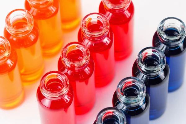 Синя, червона та помаранчева рідина в хімічних лабораторних пробірках на білому тлі — стокове фото