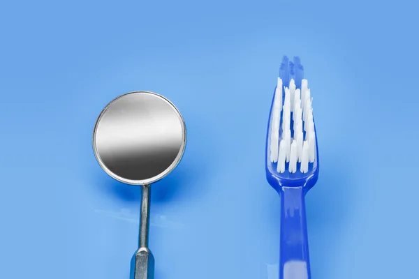 Espejo dentista y cepillo de dientes sobre un fondo azul — Foto de Stock