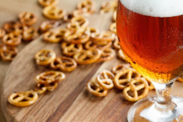 A glass of cold foamy beer with pretzels. Traditional german Oktoberfest snacks and beer on wooden background