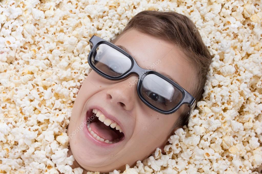 Laughing young boy in stereo glasses looking out of popcorn
