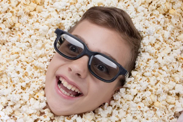 Смеющийся мальчик в стерео очках, выглядывающий из попкорна. — стоковое фото