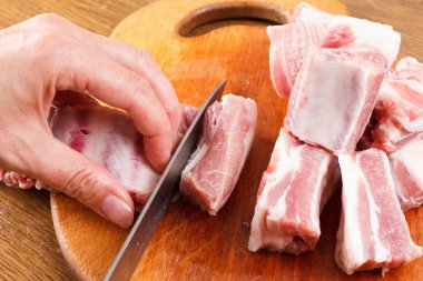 chef knife cuts raw pork ribs on a cutting board clipart