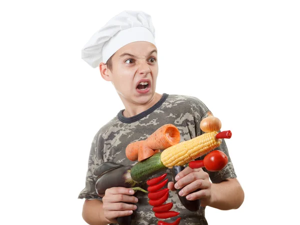 Humorous portrait of a teen boy chef with rifle vegetables, white background — Stock Photo, Image