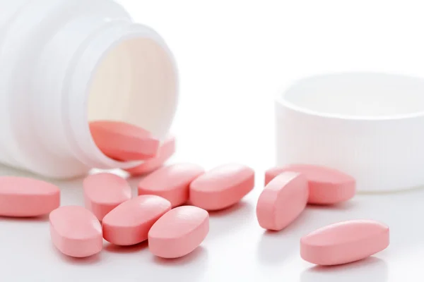 Pink oval pills poured out of a white bottle — Stock Photo, Image