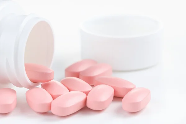 Varias píldoras ovaladas rosadas derramadas de un frasco blanco — Foto de Stock