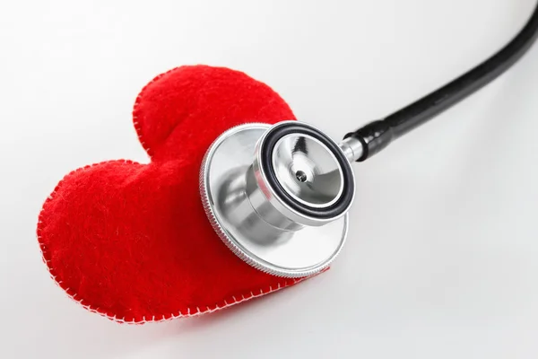 Corazón rojo y un estetoscopio sobre fondo blanco — Foto de Stock