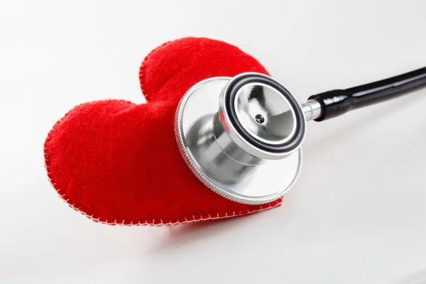 Corazón rojo y un estetoscopio sobre fondo blanco — Foto de Stock