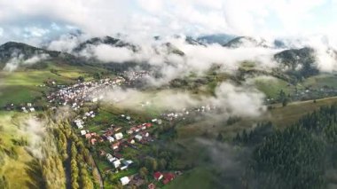 Yeşil tepelerle çevrili bir dağ köyünü ve yağmurdan sonra sürüklenen sisi hava hızıyla yakalıyor. Alçak bulutlar vadide usulca hareket eder, yumuşak sabah ışığı altında çatılar ve ormanlar ortaya çıkar.
