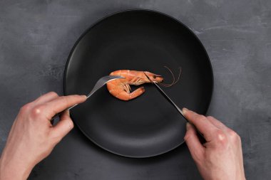 Gri üzerine siyah tabakta büyük bir karides. Sağlıklı deniz ürünleri. Minimalizm, keto zayıflama diyet konsepti. Üst Manzara. Çatal ve bıçak tutan adam elleri.