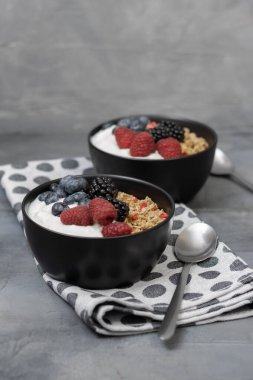 İçinde yoğurt ve koyu gri arka planda siyah kasede taze böğürtlen olan müsli. Sağlıklı kahvaltı..