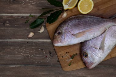 Limon dilimleri, otlar ve mavi ahşap arka planda sarımsakla süslenmiş taze çiğ deniz Dorada. Sağlıklı gıda kavramı, üst görünüm, kopyalama alanı
