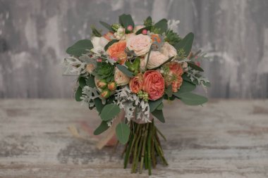 Beyaz ve turuncu gül buketi, frezya ve okalipus, uzun ipek kurdele ile süslenmiş gri dokuma arka planda yatıyor..