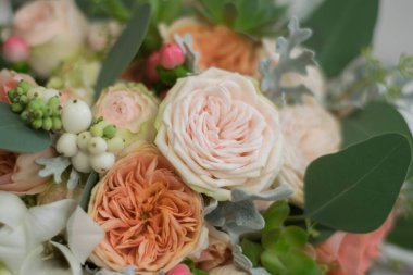 Beyaz ve turuncu gül buketi, frezya ve okalipus, uzun ipek kurdele ile süslenmiş gri dokuma arka planda yatıyor..