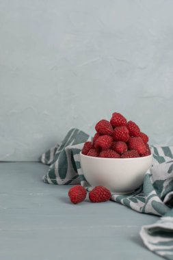 Açık mavi taşlı arka planda küçük beyaz bir kasede ahududu. Taze meyve..