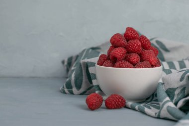 Açık mavi taşlı arka planda küçük beyaz bir kasede ahududu. Taze meyve..