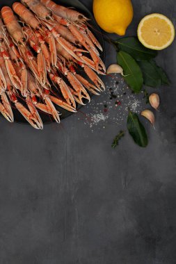 Siyah tabakta kaynamış Langoustines gri beton masada izole edilmiş. Limon ve baharatlı otlarla servis edilir..