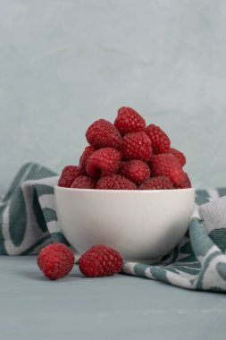 Açık mavi taşlı arka planda küçük beyaz bir kasede ahududu. Taze meyve..