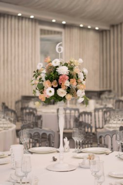 Masanın üzerinde yeşil yapraklar ve taze çiçeklerden yapılmış bir süs duruyor. Düğün günü. Taze çiçek süslemeleri. Şeftali ve beyaz takoz dekorasyonları.