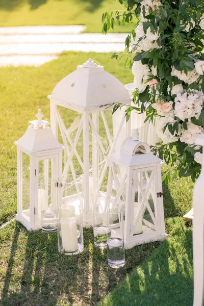 Wedding decor in rustic style.Two white vintage lamp with flowers inside standing on green grass. Wedding day.