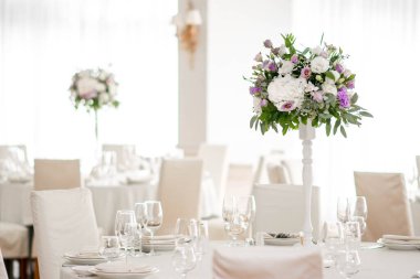 Masanın üzerinde yeşil yapraklar ve taze çiçeklerden yapılmış bir süs duruyor. Düğün günü. Taze çiçek süslemeleri. Şeftali ve beyaz takoz dekorasyonları.