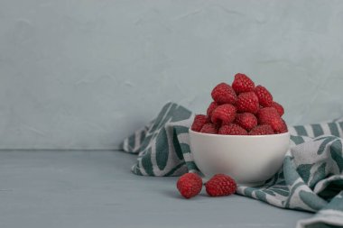 Açık mavi taşlı arka planda küçük beyaz bir kasede ahududu. Taze meyve..