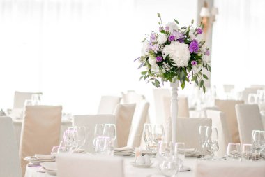 Masanın üzerinde yeşil yapraklar ve taze çiçeklerden yapılmış bir süs duruyor. Düğün günü. Taze çiçek süslemeleri. Şeftali ve beyaz takoz dekorasyonları.
