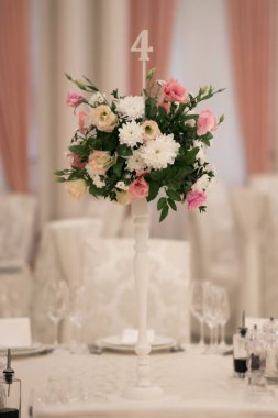 Masanın üzerinde yeşil yapraklar ve taze çiçeklerden yapılmış bir süs duruyor. Düğün günü. Taze çiçek süslemeleri. Şeftali ve beyaz takoz dekorasyonları.