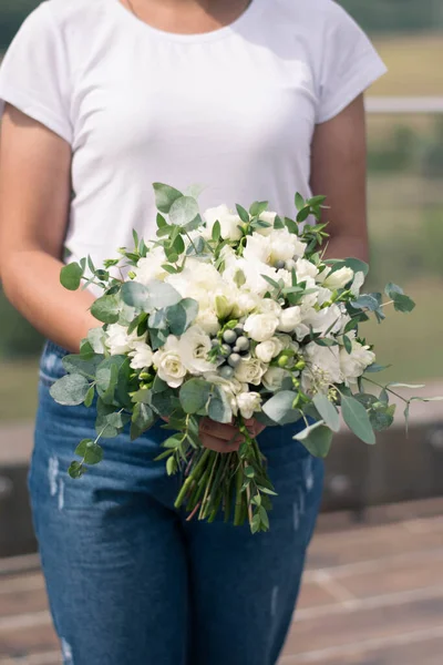 Florist hands holding modern bridal bouquet of white flowers and greenery. Wedding bouquet composed of roses, freesia, lisianthus, brunia and eucalyptus. Wedding day.