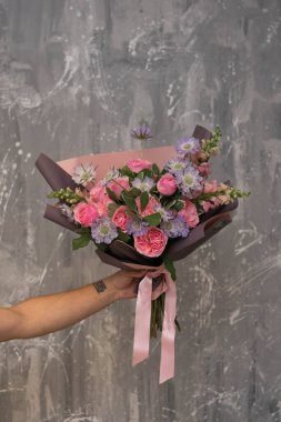 Erkek el, büyük ve güzel bir buket taze çiçeği pembe ve mavi renkte tutuyor, kırpılmış fotoğraf, buketi yakın.