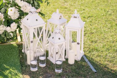 Kırsal tarzda düğün dekoru. İçinde çiçekler olan iki beyaz klasik lamba yeşil çimlerin üzerinde duruyor.