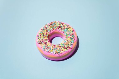 Pink bright frosted donut with colorful sprinkles and pink glaze on grey faded background. Minimal food sunlit lay out.