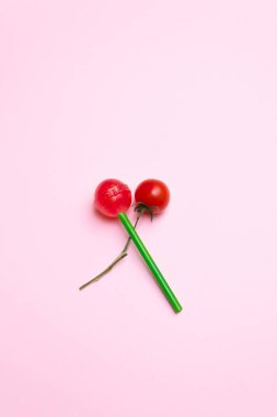 Fresh cherry tomato and red lollipop with green stick crossed against pastel pink and violet background. Minimal flat lay food concept.