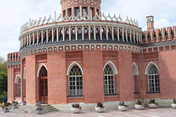 Görkemli, kırmızı tuğlalı bir binanın Gotik canlandırma tasarımının detaylı bir ön görüntüsü. Sivri uçlu kemerli pencereler, kuleleri olan beyaz dekoratif bir korkuluk ve halka açık bir meydanda kurulu merkezi ahşap bir kapı yer alıyor..