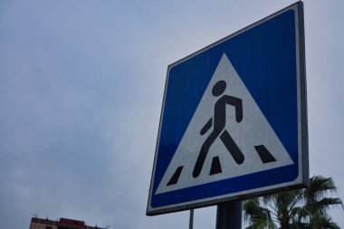 Mavi Yayalar Gri Gökyüzüne Karşı Trafik İşareti, Kare Yol Güvenliği Sinyali Yürüyen Kişiler Sembolü, Şehir Altyapısının Yakın Çekimi ve Yerleşim Alanında Yol Bulma