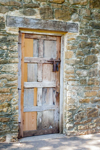 Porta de madeira multicolorida contra parede de pedra Worn — Fotografia de Stock