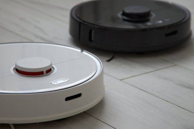 Siyah beyaz robot elektrikli süpürgeler yerleri temizliyor.