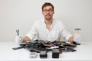 Bir akıllı telefon tamircisi büyük bir bozuk telefon yığınını tamir etmekten mutluluk duyar..