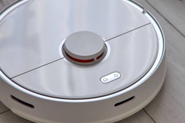 Beyaz robot elektrikli süpürge zemini temizliyor.