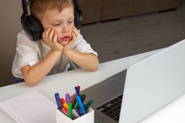 Kulaklıklı bir çocuk dizüstü bilgisayarın önünde otururken başını dinlendirdi.