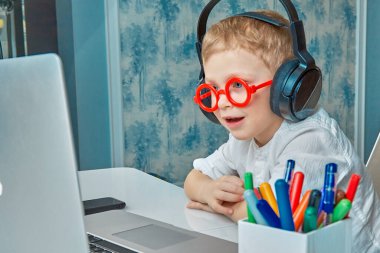 Kulaklıklı çocuk bir dizüstü bilgisayarla iletişim kurarken gülümsüyor.