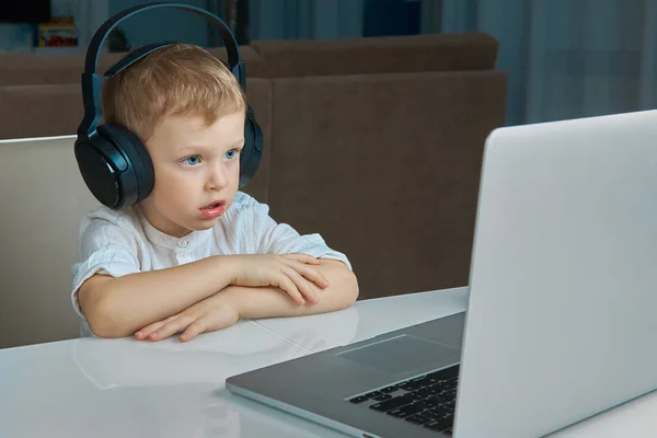 Το αγόρι με τα ακουστικά κοιτάζει προσεκτικά την οθόνη του φορητού υπολογιστή. — Φωτογραφία Αρχείου