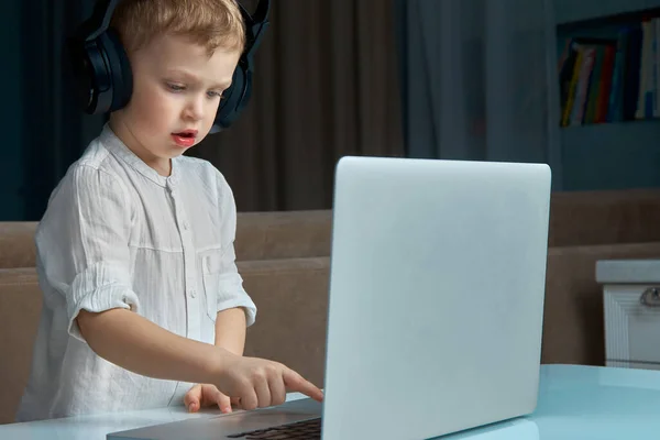 A blond boy with headphones is learning to type on a laptop keyboard. — Stock Photo, Image