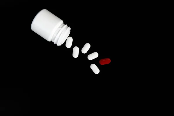 一个白色的罐子，有分散的药丸在黑色的背景上 — 图库照片