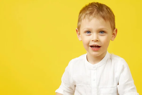 Retrato de un pequeño niño feliz de ojos azules sobre un fondo amarillo — Foto de Stock