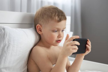 Uykulu mavi gözlü tatlı çocuk yatmadan önce cep telefonu kullanıyor.