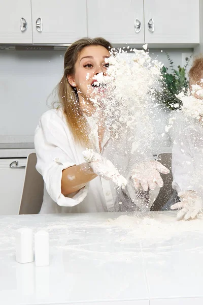 A happy girl in a white kitchen throws flour in the air — Stock Photo, Image