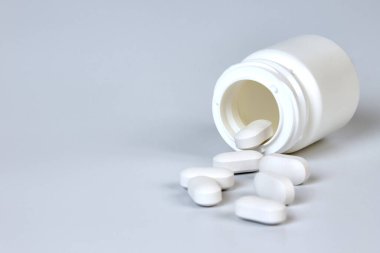 Gri arka planda dağınık tabletlerle dolu bir şişe.