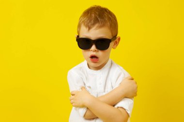 Kollarını kavuşturmuş güneş gözlüklü bir çocuk poz veriyor.