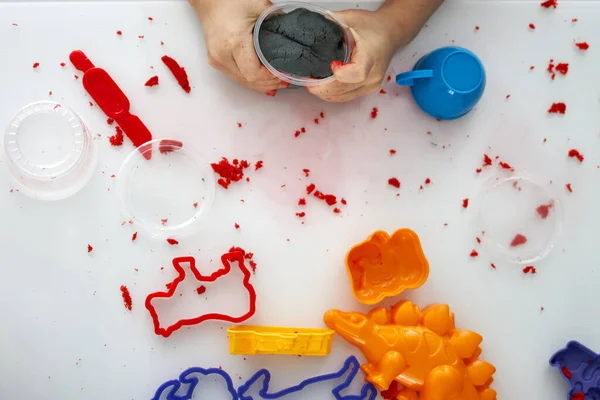 A childs hands play with kinetic sand on a white table